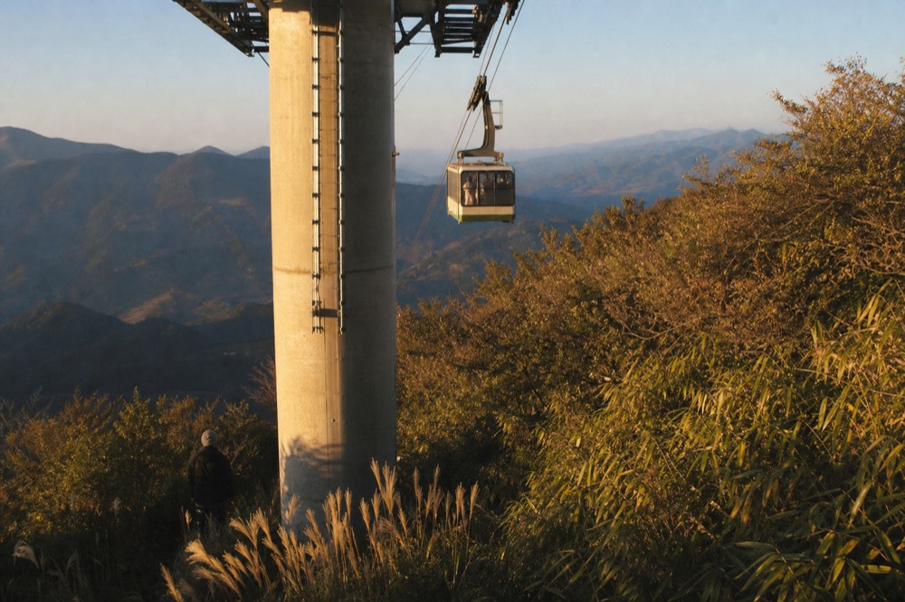 Gondola cabins passing a tower column on a hillside above Taipei, no text, no logos, no people