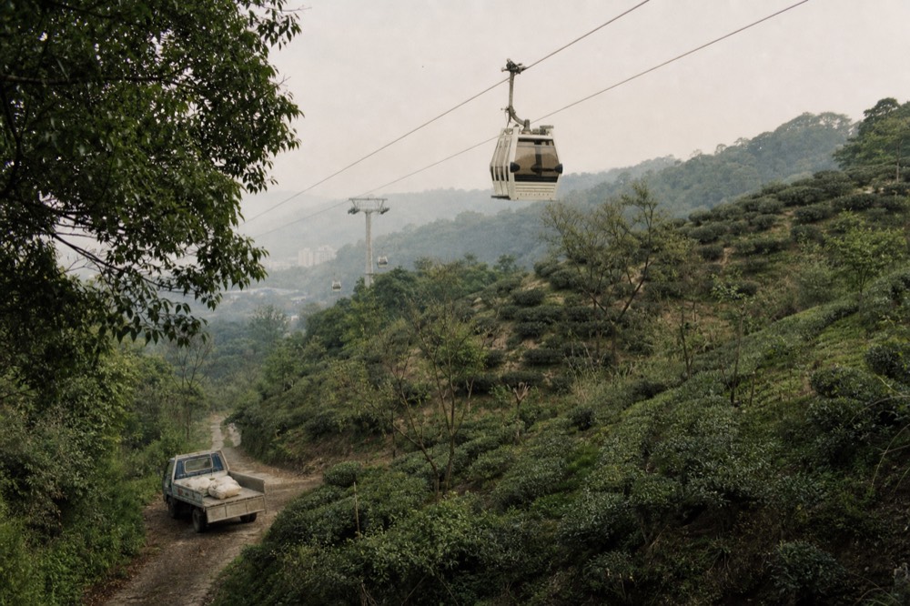 A passenger holding a phone with a booked gondola ticket beside a cable car station entrance, no text, no logos, no people