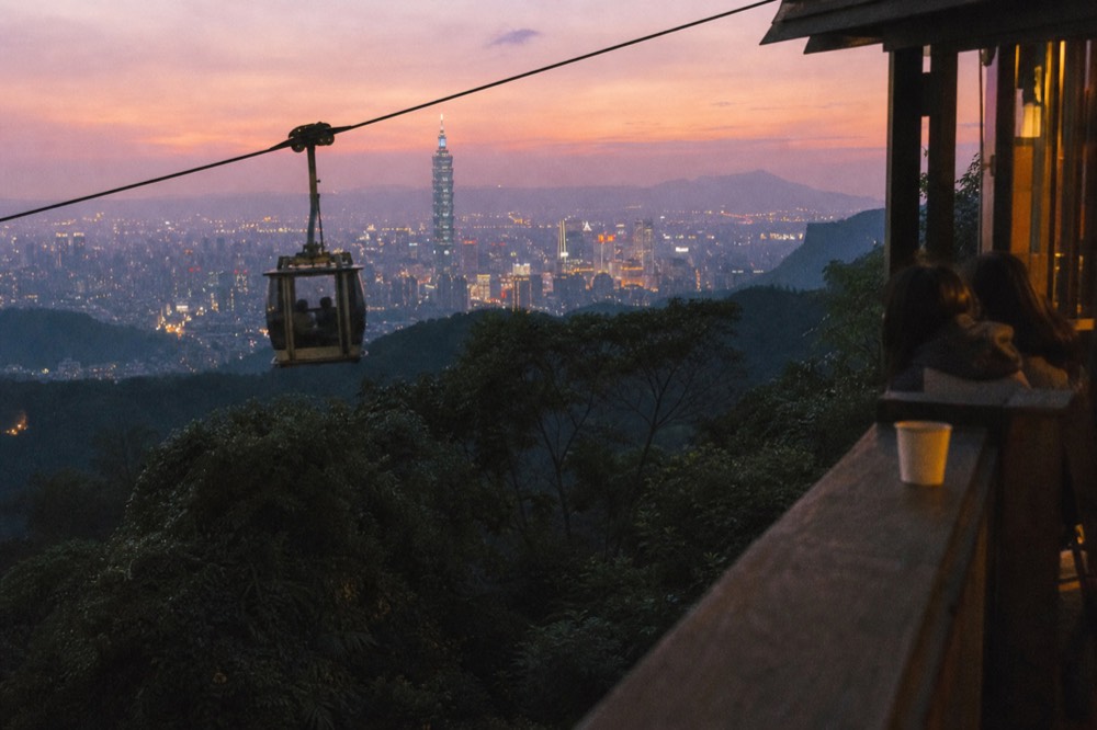 A gondola cabin silhouetted against a wide view over the Taipei basin at dusk, no text, no logos, no people