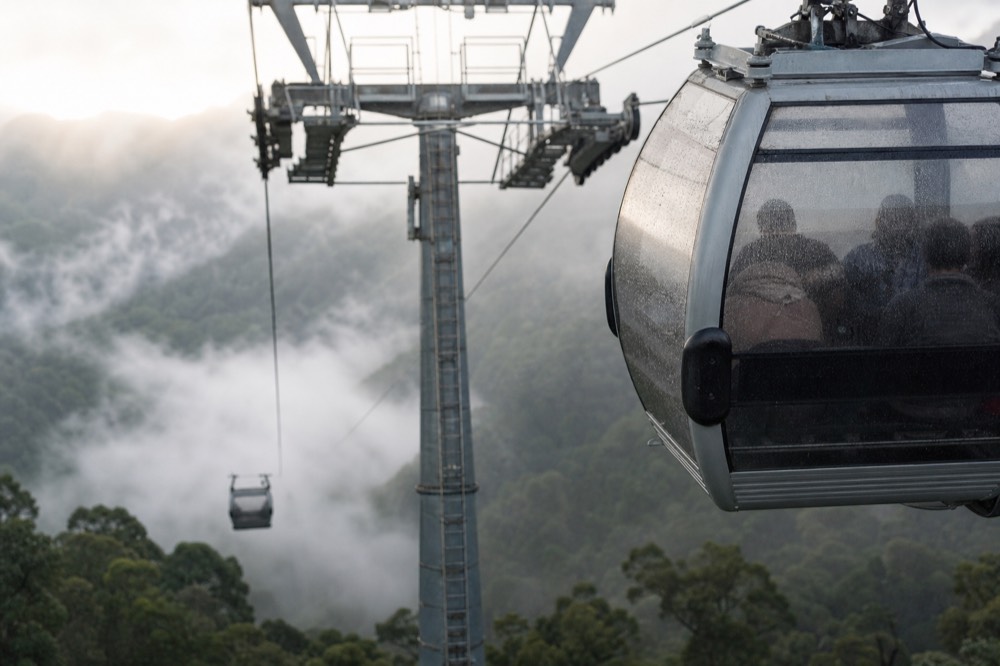 A gondola cabin passing a support tower above a forested valley, no text, no logos, no people