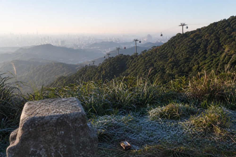 A cable car line curving across a green ridge with city buildings far below, no text, no logos, no people
