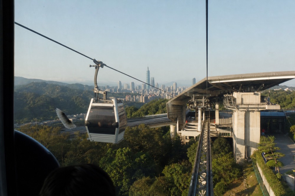 Gondola cabins arriving at Taipei Zoo Station above the MRT entrance, no text, no logos, no people
