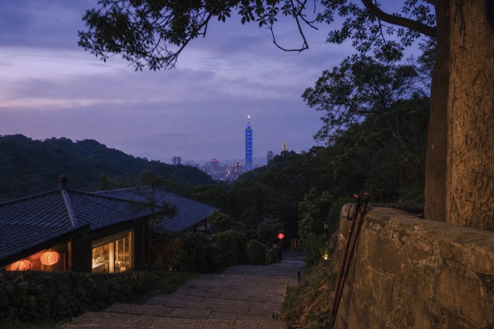 Taipei 101 tower rising over the evening city skyline seen from a hillside, no text, no logos, no people