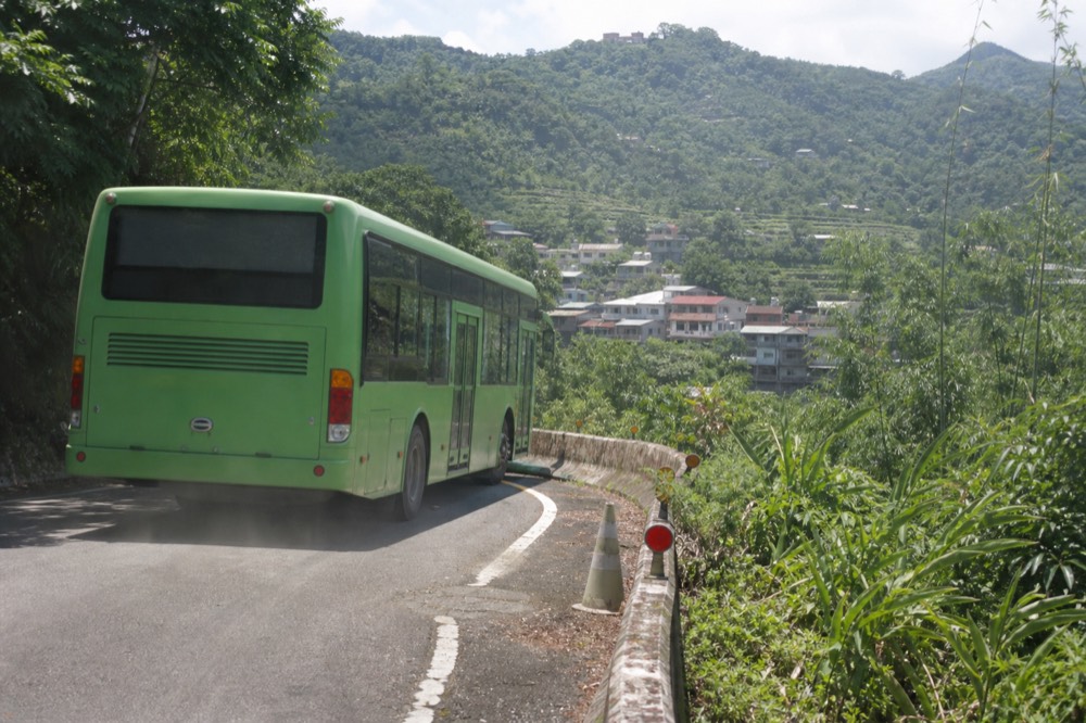 A Taipei city bus on a narrow mountain road above tea fields, no text, no logos, no people