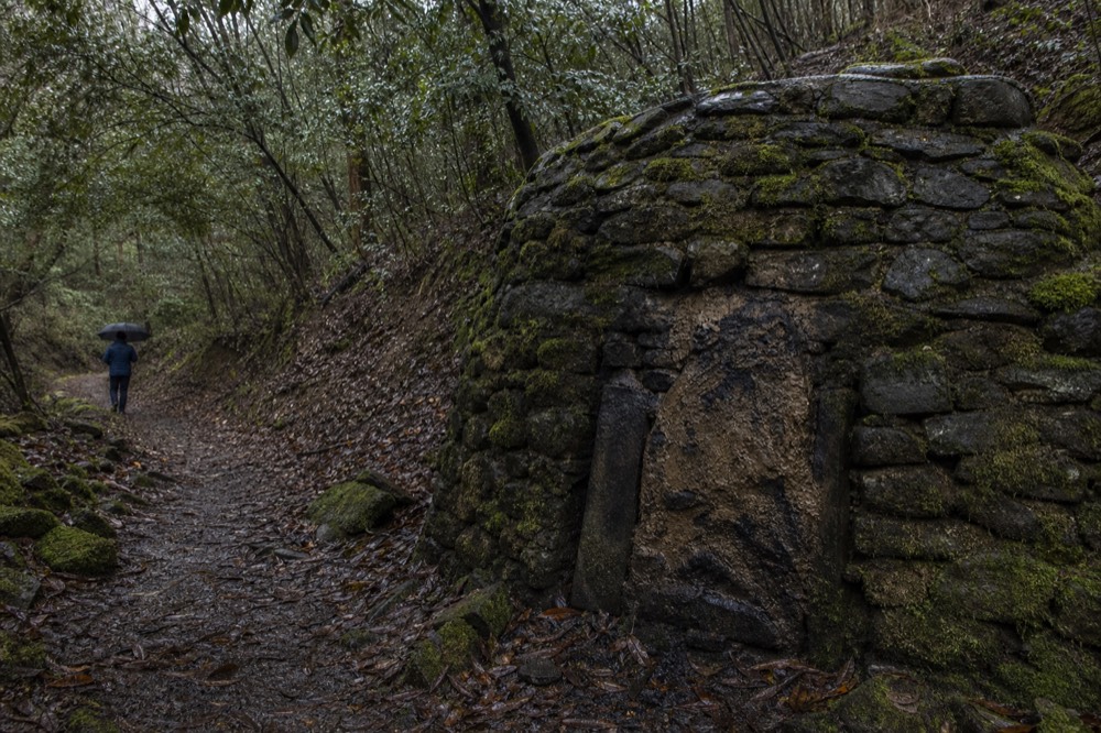 A restored stone and clay charcoal kiln on a forested hillside trail, no text, no logos, no people
