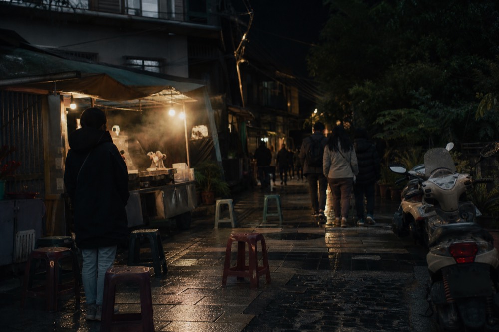 Taipei streetscape at night with food stalls glowing along a busy lane, no text, no logos, no people