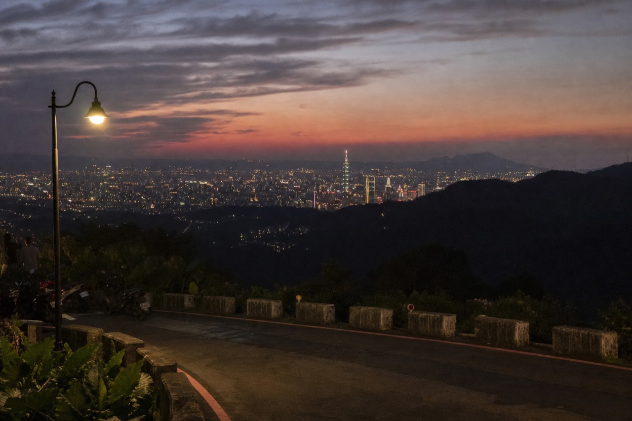 Taipei city skyline at dusk with forested hills rising behind the towers, no text, no logos, no people