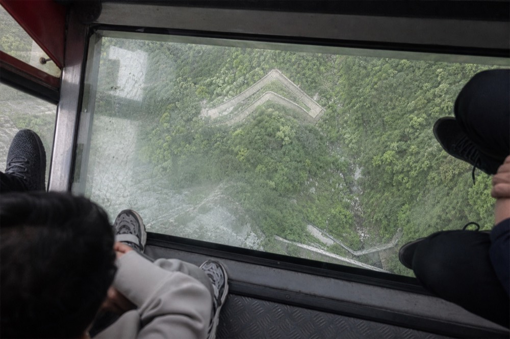 Interior of a glass-floor cable car cabin showing the valley below through the transparent floor, no text, no logos, no people