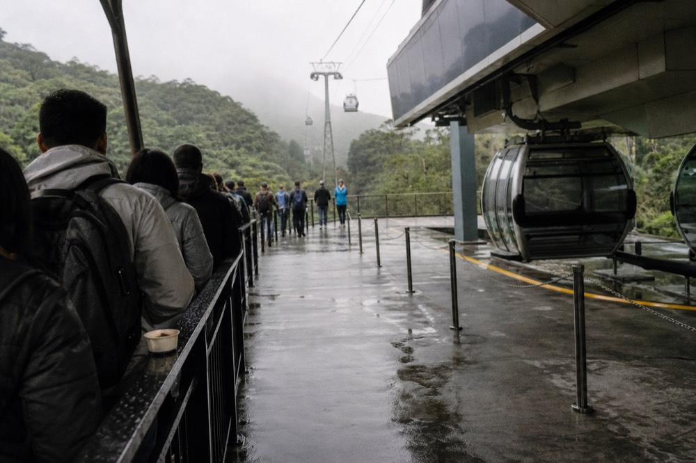Queue area at a cable car station with a separate glass-floor cabin boarding line, no text, no logos, no people