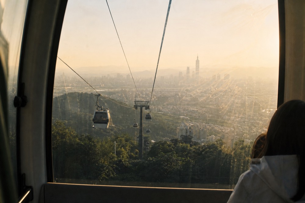 Cable car cabin climbing above the Taipei city skyline in late afternoon light, no text, no logos, no people