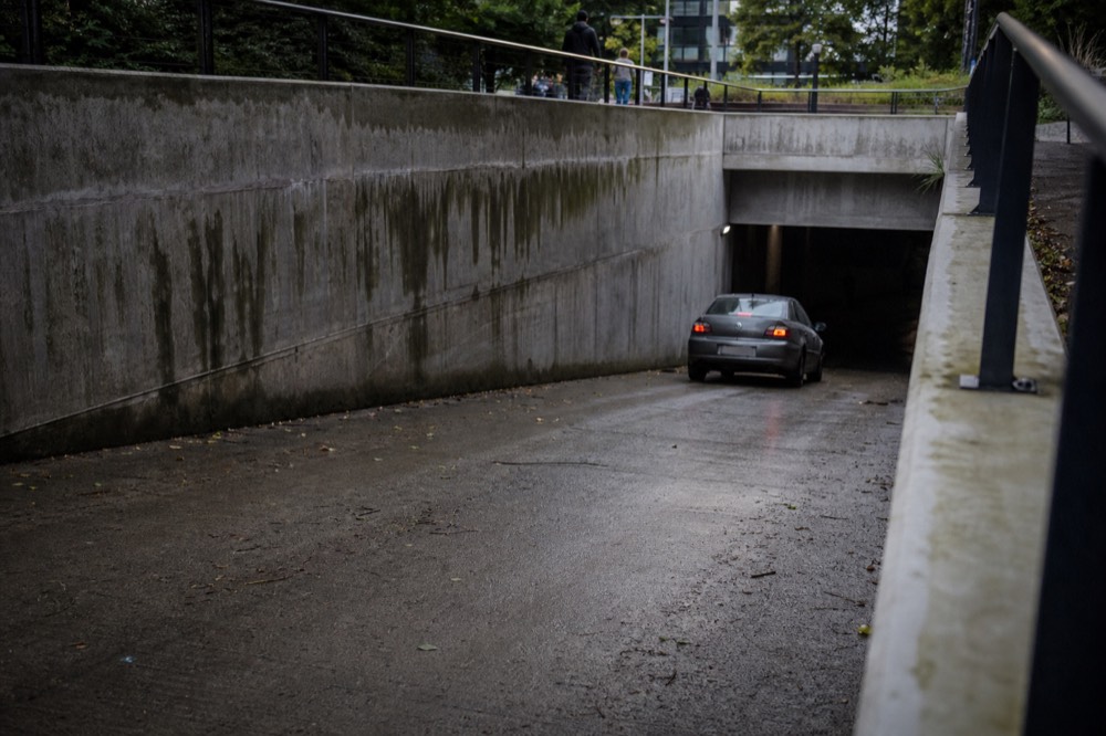Entrance ramp of an underground car park beside a green hillside station, no text, no logos, no people