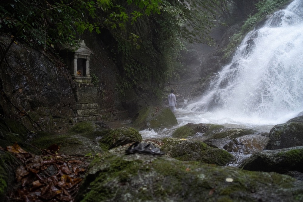 A waterfall falling past a small cliff-face shrine in a green gorge, no text, no logos, no people