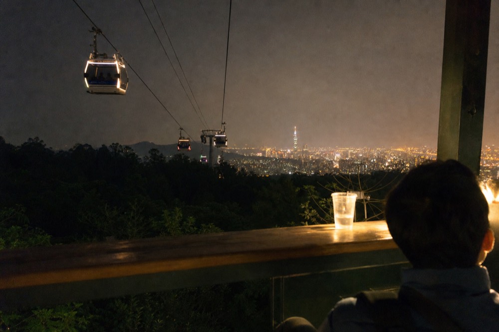 Gondola cabins gliding over darkened forest with Taipei city lights glowing in the valley below, no text, no logos, no people