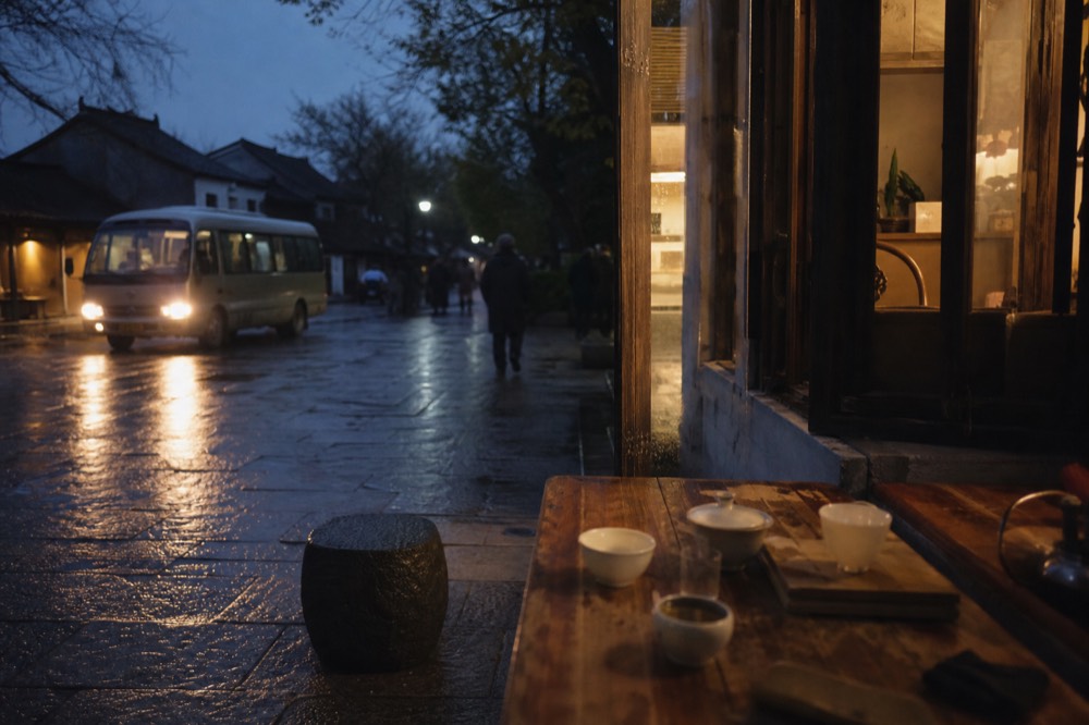 Shuttle bus waiting at a mountain station curb near tea houses at dusk, no text, no logos, no people
