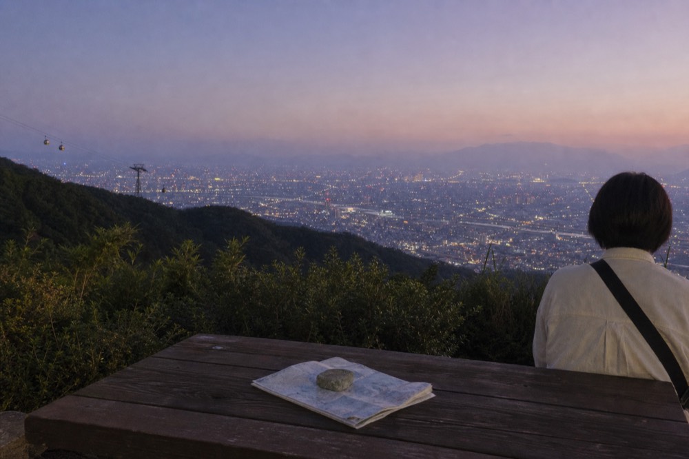 Wide view of the Taipei basin at dusk with gondola cables faintly crossing the darkening hillside, no text, no logos, no people