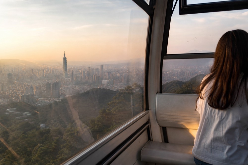 View from inside a gondola cabin over the Taipei basin during the ascent, no text, no logos, no people