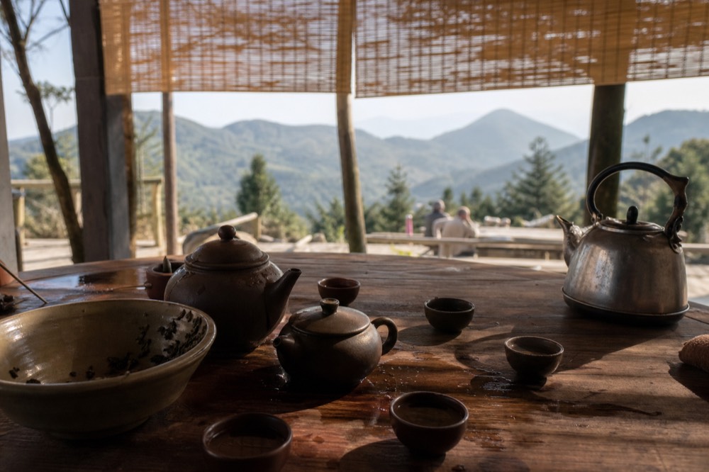 Tea pots and cups arranged on a wooden table beside a valley view, no text, no logos, no people