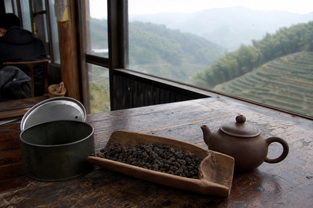 Roasted dark oolong tea leaves in a wooden scoop beside a clay teapot, no text, no logos, no people