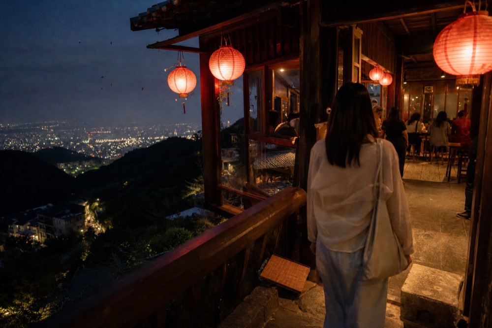 Lantern-lit terrace of a hillside tea house at dusk above city lights, no text, no logos, no people