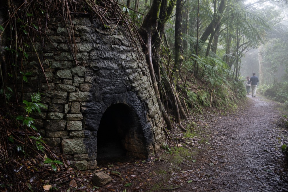 A restored stone charcoal kiln beside a forested walking trail, no text, no logos, no people